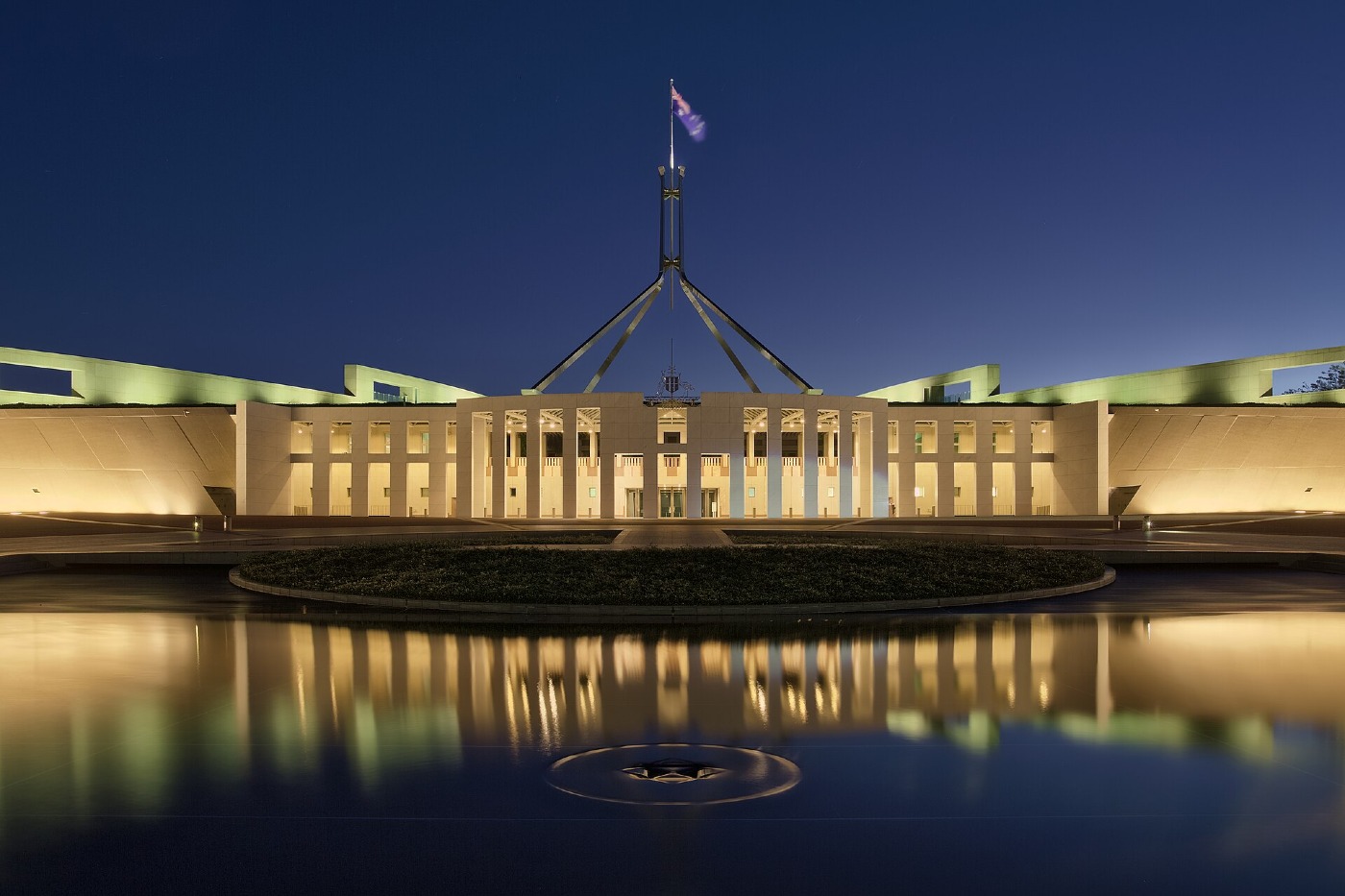 Parliament House in Canberra at dusk, lit up and reflected in water