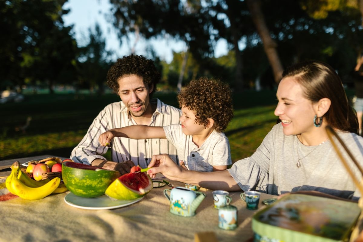 A family sharing a picnic of fruit in a sunny park